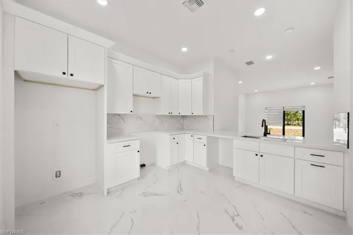 Kitchen featuring recessed lighting, light marble finish floors, white cabinetry, and decorative backsplash