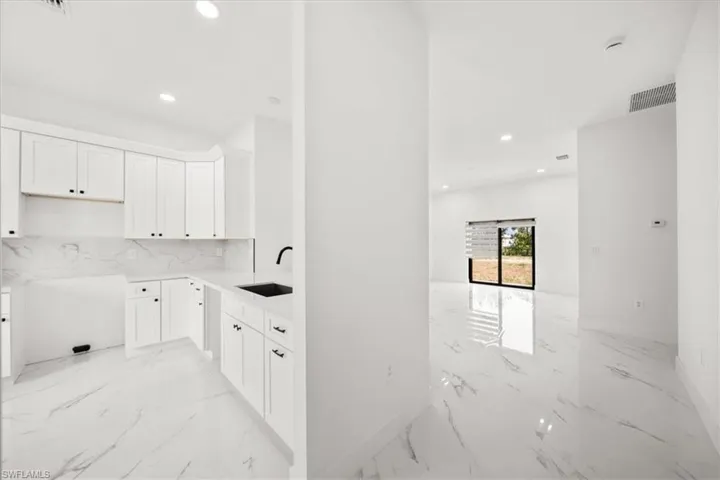 Kitchen featuring light marble finish floors, recessed lighting, tasteful backsplash, white cabinets, and open floor plan