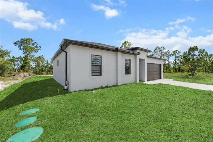View of front of house with an attached garage, concrete driveway, a front yard, and stucco siding