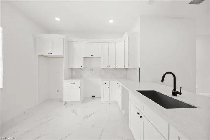 Kitchen featuring white cabinets, recessed lighting, light marble finish flooring, light stone countertops, and backsplash