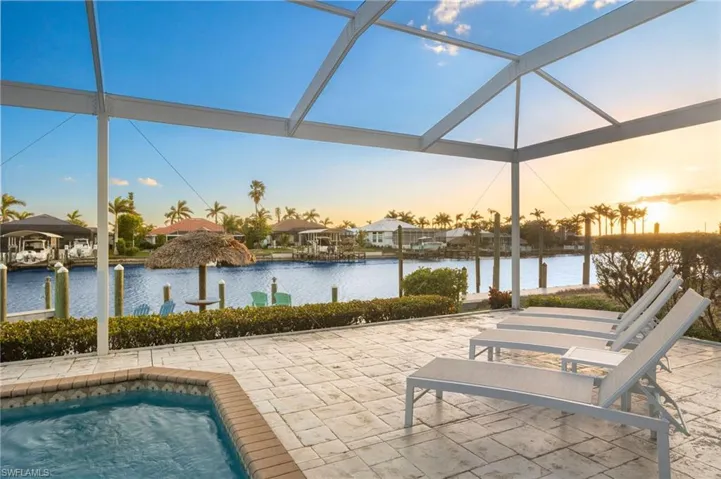Pool at dusk with a water view, glass enclosure, and a patio area