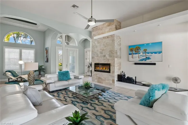 Living room with ceiling fan with notable chandelier, light tile patterned floors, a fireplace, and a high ceiling