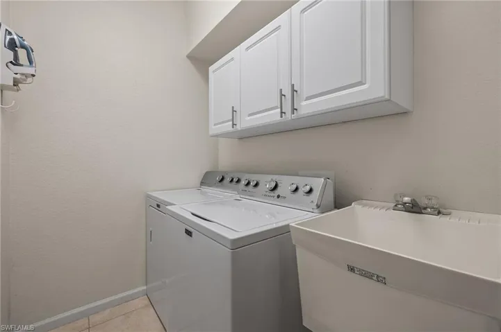 Laundry room featuring light tile patterned flooring, cabinets, independent washer and dryer, and sink