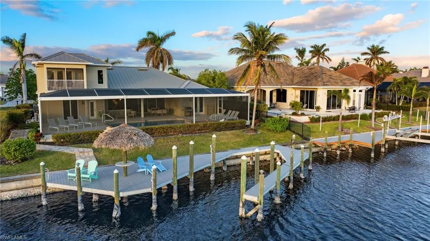 Back house at dusk featuring a patio, a pool, a water view, and glass enclosure