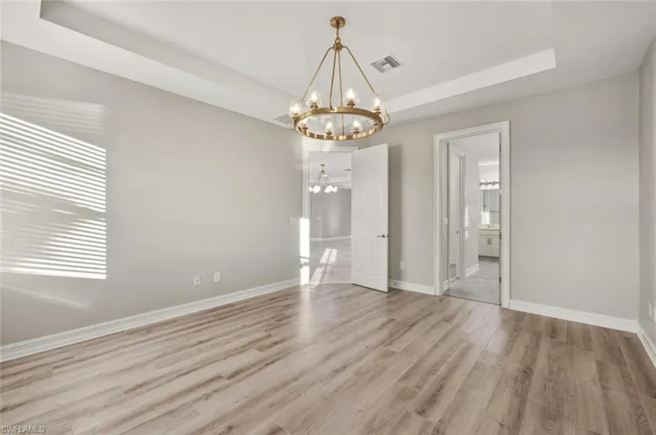 Unfurnished dining area with light wood-style floors, a raised ceiling, and a chandelier