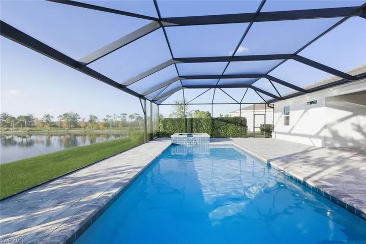 View of pool featuring a water view, a sunroom, a pool with connected hot tub, a lawn, and a lanai