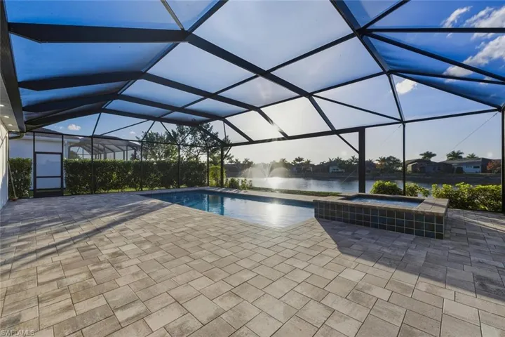 View of pool featuring a sunroom, glass enclosure, a water view, a patio, and a pool with connected hot tub