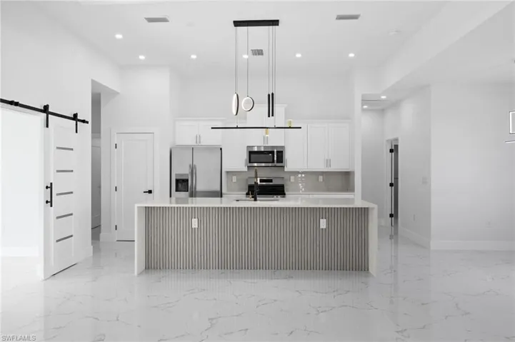 Kitchen featuring a barn door, a towering ceiling, white cabinetry, stainless steel appliances, and a large island