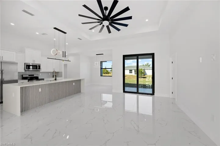 Kitchen with white cabinets, stainless steel appliances, a large island, light marble finish flooring, and a tray ceiling