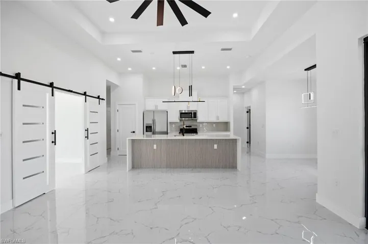 Kitchen featuring a barn door, white cabinetry, a large island, a high ceiling, and appliances with stainless steel finishes