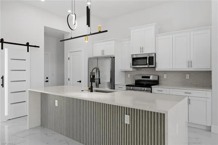 Kitchen featuring light marble finish flooring, a barn door, appliances with stainless steel finishes, and backsplash