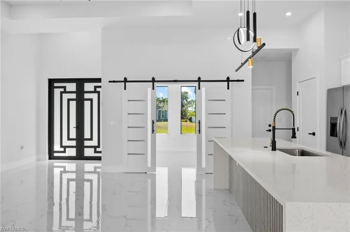Kitchen featuring light marble finish flooring, light stone counters, a barn door, stainless steel fridge with ice dispenser, and recessed lighting