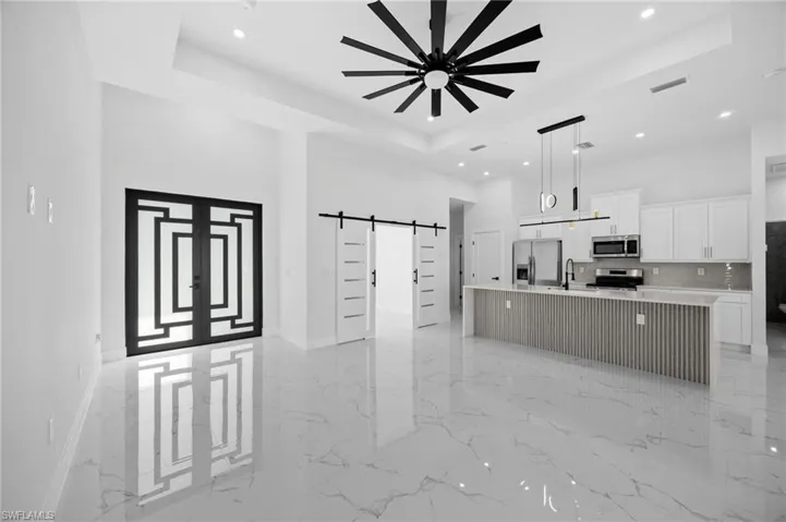 Kitchen featuring a barn door, open floor plan, white cabinets, a large island with sink, and a tray ceiling