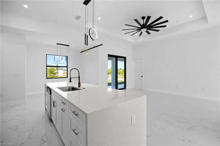 Kitchen with light marble finish floors, white cabinets, light stone countertops, pendant lighting, and a tray ceiling