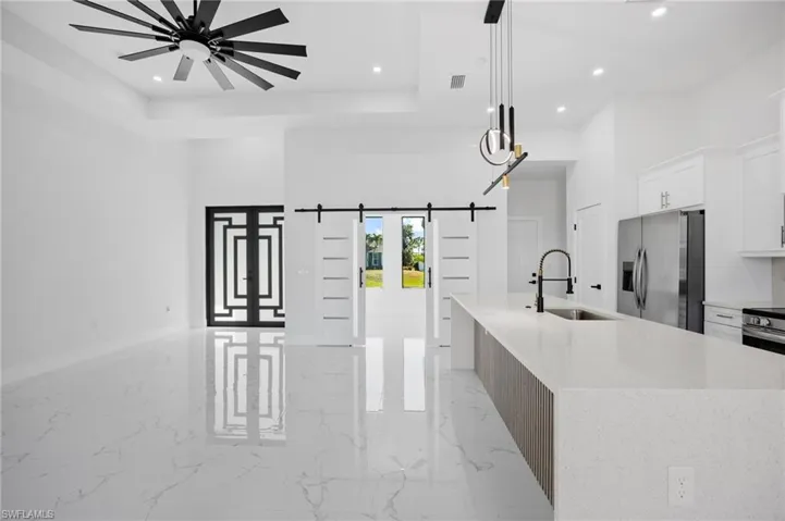 Kitchen with light marble finish floors, white cabinets, light stone countertops, hanging light fixtures, and recessed lighting