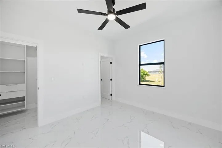 Unfurnished bedroom featuring light marble finish flooring, a walk in closet, and a ceiling fan