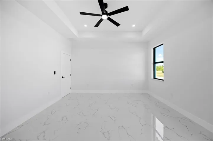 Unfurnished room featuring a tray ceiling, light marble finish flooring, a ceiling fan, and recessed lighting