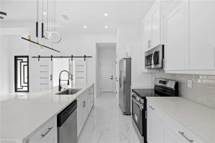 Kitchen featuring appliances with stainless steel finishes, a spacious island, light stone countertops, white cabinets, and recessed lighting