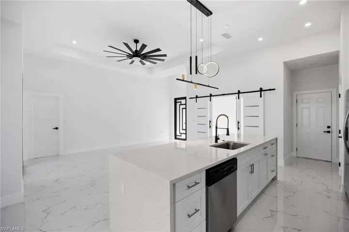 Kitchen with white cabinets, a barn door, light stone counters, dishwasher, and open floor plan
