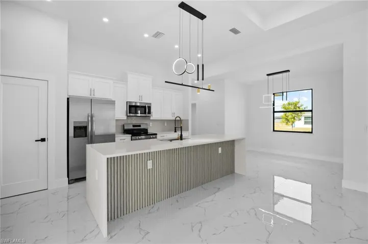 Kitchen with white cabinetry, appliances with stainless steel finishes, a large island with sink, light stone countertops, and light marble finish flooring