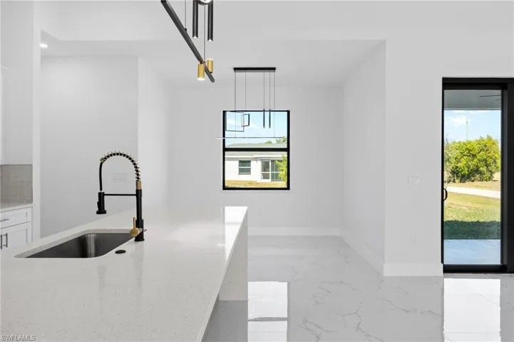 Kitchen with light stone counters, pendant lighting, light marble finish floors, and white cabinetry