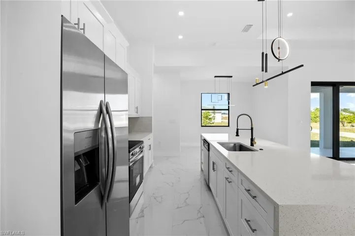 Kitchen featuring white cabinetry, stainless steel appliances, light stone counters, light marble finish floors, and a spacious island