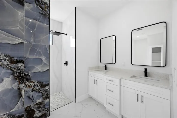 Bathroom with a marble finish shower, light marble finish flooring, and double vanity