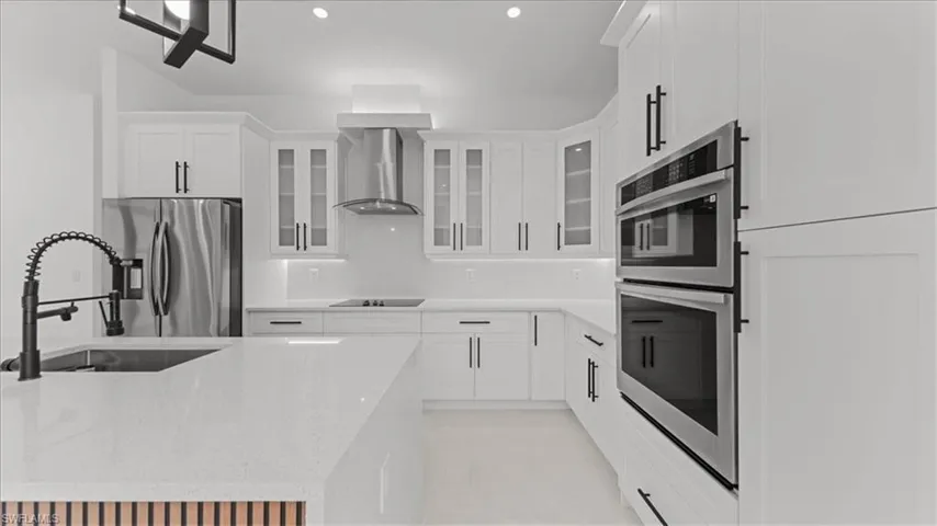 Kitchen featuring light stone countertops, stainless steel appliances, glass insert cabinets, recessed lighting, and white cabinets