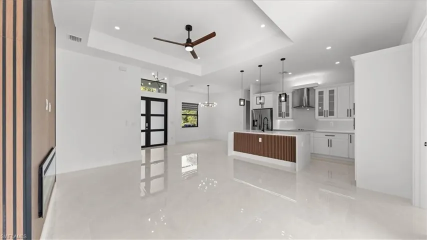 Unfurnished living room featuring a raised ceiling, a ceiling fan, recessed lighting, a chandelier, and light tile patterned floors