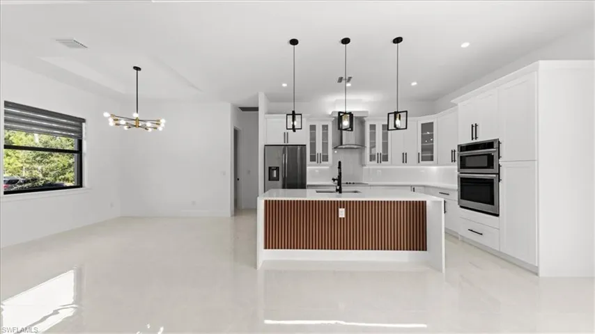 Kitchen featuring glass insert cabinets, an island with sink, white cabinetry, stainless steel appliances, and pendant lighting