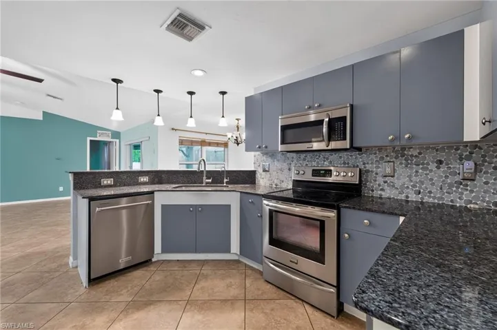Well-appointed kitchen featuring granite countertops, stainless steel appliances, modern cabinetry, and a stone mosaic backsplash