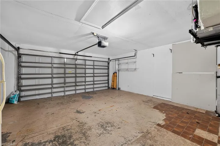 Attached garage featuring a sectional overhead door with opener, exposed framing, and existing shelving