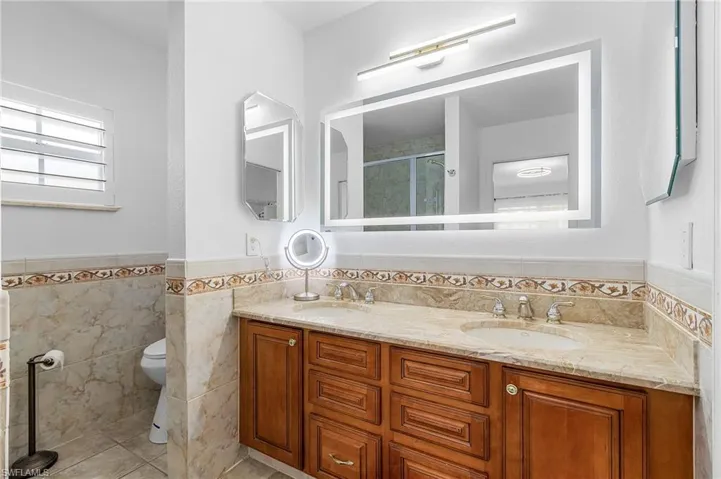 Full bathroom featuring tile walls, a wainscoted wall, double vanity, tile patterned flooring, and a stall shower