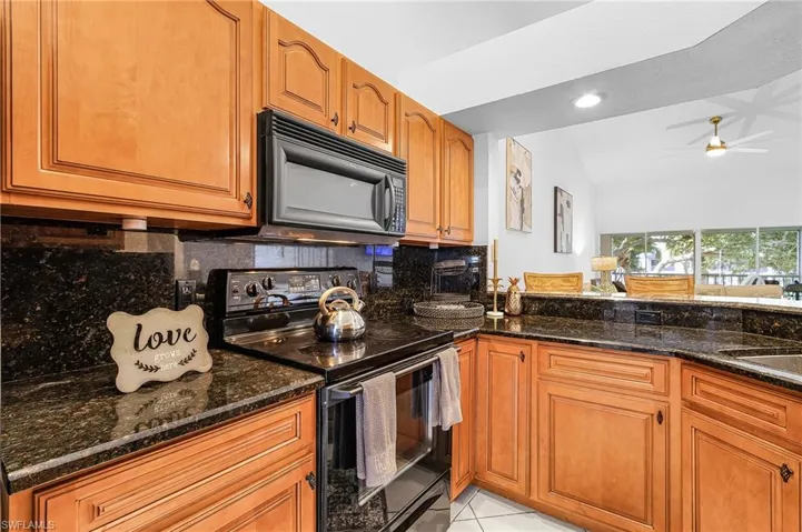 Kitchen with decorative backsplash, black appliances, dark stone counters, vaulted ceiling, and a ceiling fan