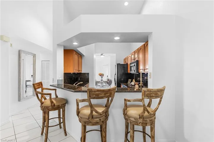 Kitchen featuring tasteful backsplash, light tile patterned flooring, a breakfast bar area, a peninsula, and black microwave