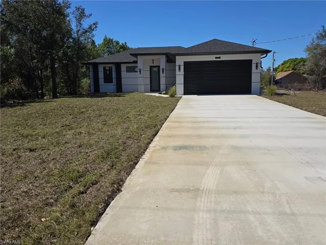 View of front of house with a front yard, a garage, driveway, and a shingled roof