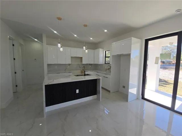 Kitchen featuring modern cabinets, a kitchen island with sink, white cabinetry, and light stone countertops