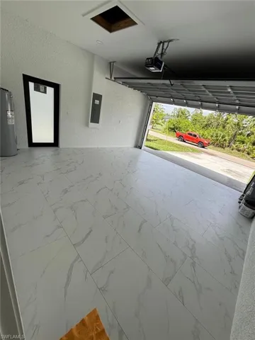 Garage featuring a textured wall, water heater, electric panel, and a garage door opener