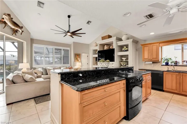 Kitchen with dark stone counters, black appliances, ceiling fan, light tile patterned flooring, and sink
