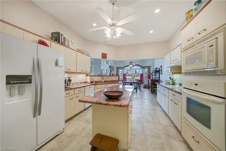 Kitchen with white appliances, a kitchen island, ceiling fan, white cabinets, and decorative backsplash