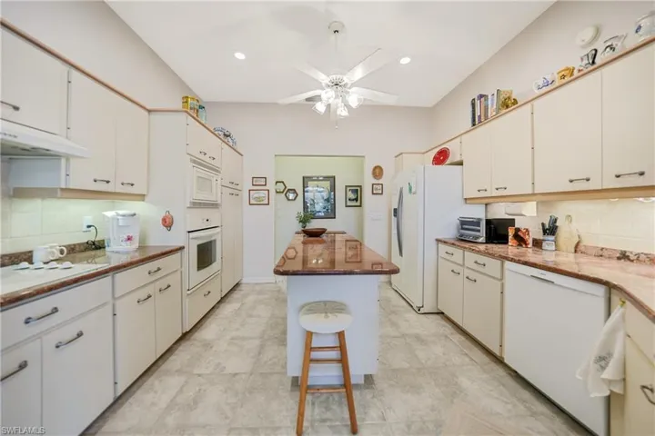 Kitchen featuring a kitchen island, white cabinets, decorative backsplash, and white appliances