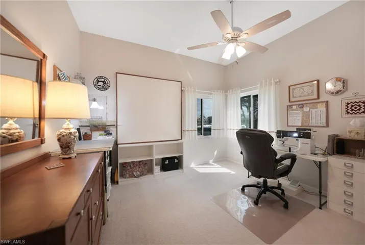 Carpeted office with lofted ceiling and ceiling fan