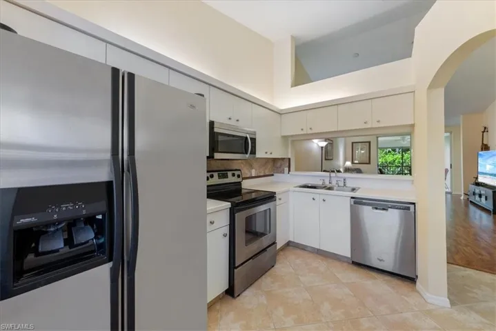 Kitchen with light countertops, arched walkways, white cabinets, a sink, and stainless steel appliances