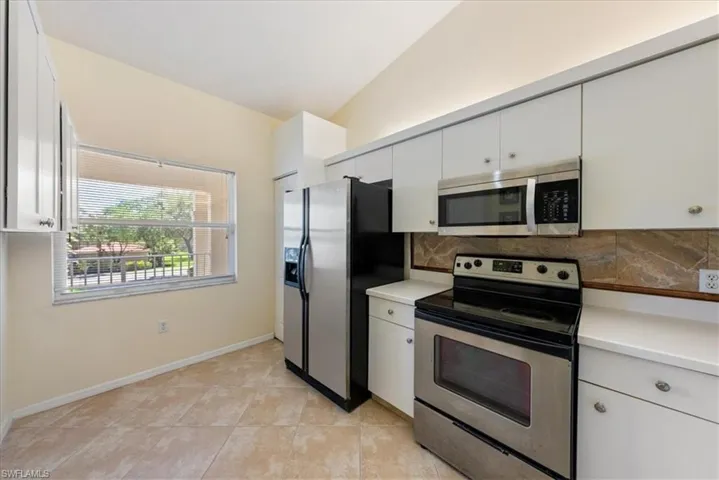 Kitchen featuring decorative backsplash, baseboards, light countertops, white cabinetry, and stainless steel appliances