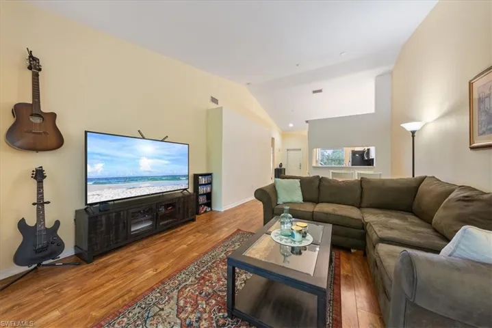 Living area with baseboards, visible vents, wood finished floors, and lofted ceiling