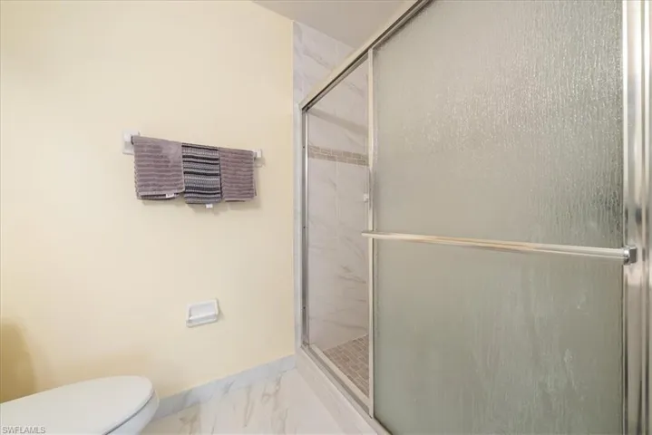 Bathroom with baseboards, marble finish floor, a stall shower, and toilet