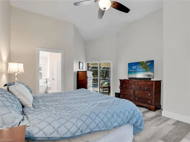 Primary bedroom featuring ceiling fan, high vaulted ceiling, luxury vinyl flooring, ensuite bathroom, and access to lanai