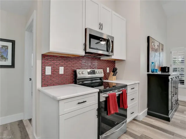 Kitchen featuring light hardwood / wood-style flooring, decorative backsplash, white cabinets, and stainless steel appliances