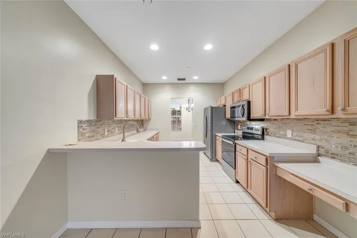 Kitchen featuring light brown cabinets, stainless steel appliances, light countertops, a peninsula, and recessed lighting