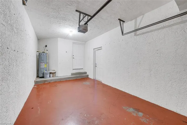 Garage with a textured wall, water heater, and a garage door opener